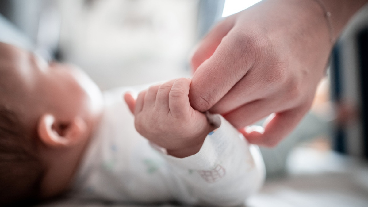 Ein Baby klammert sich an den Finger seiner Mutter. - dpa