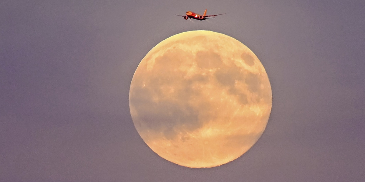 Ein Flugzeug fliegt vor dem sogenannten Supermond am frühen Abend über Leipzig.